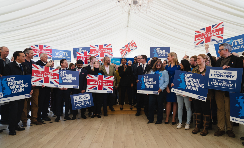 A Conservative Party campaign rally in Essex with Leader of the Conservative Party Kemi Badenoch MP and Shadow Secretary of State for Housing, Communities and Local Government Sir James Cleverly MP, surrounded by activists holding signs reading “Get Britain Working Again”, “Stronger High Streets”, “Vote Conservative”, and “Stronger Economy, Stronger Country”.